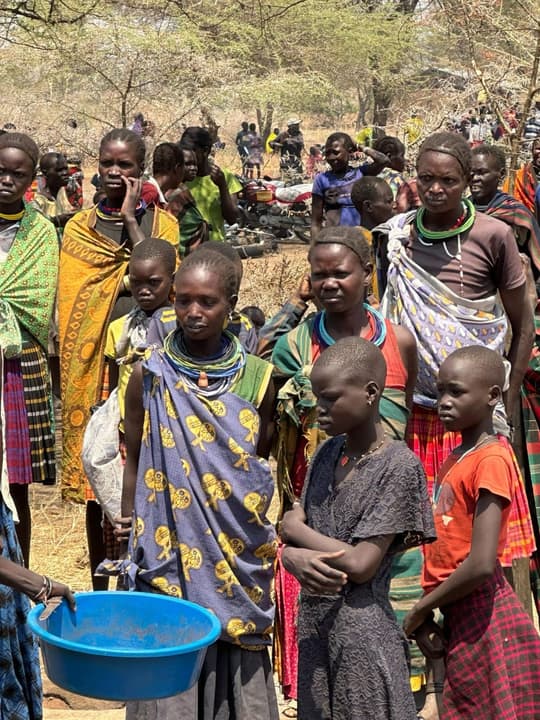 Women and children gathered at the distribution point, one holding a blue basin
