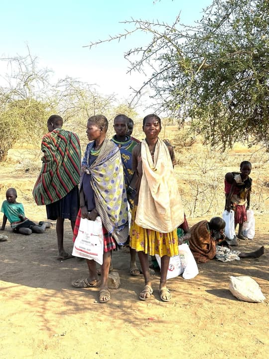 Women in traditional shawls in the dry bush, their aid bags at their feet