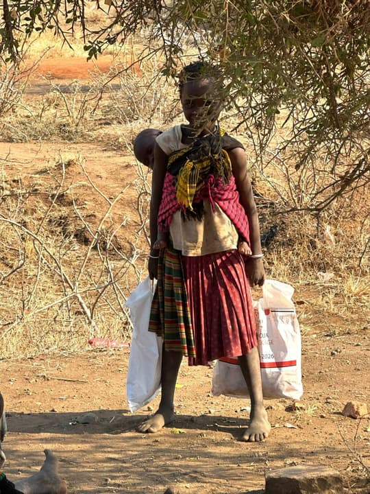 A young mother carries her child on her back and an aid bag in each hand