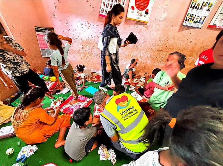 Learning games and flashcards with children at a shelter, alongside a LëtzHelp volunteer